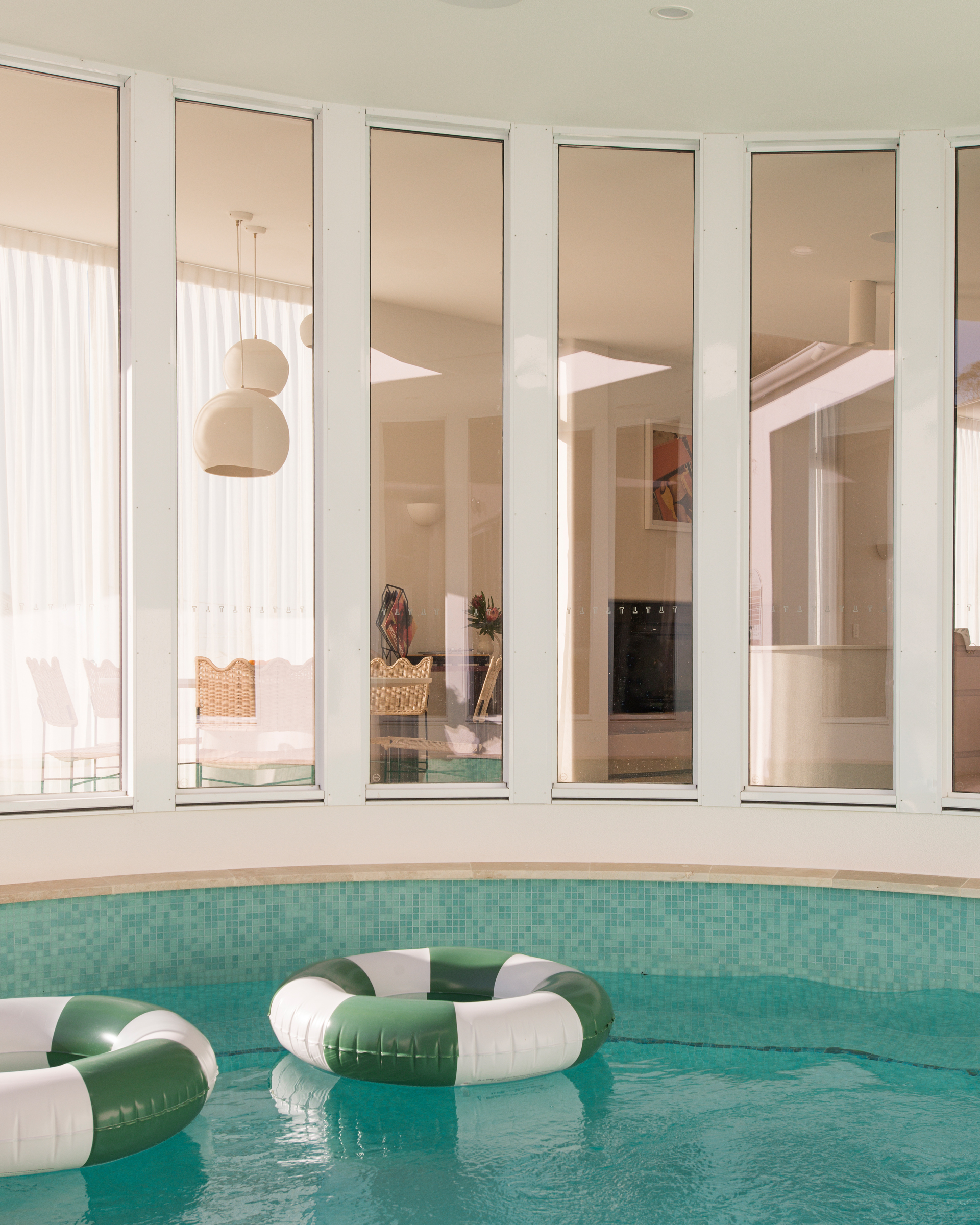 blue outdoor pool with 5 window panels overlooking dining room with white ceramic pendants