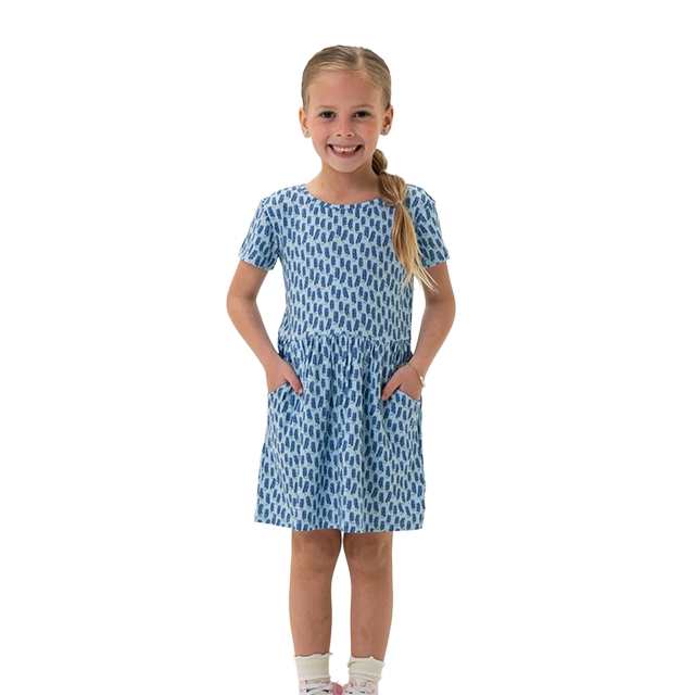 Smiling girl in blue patterned dress with pockets, standing against a white background.