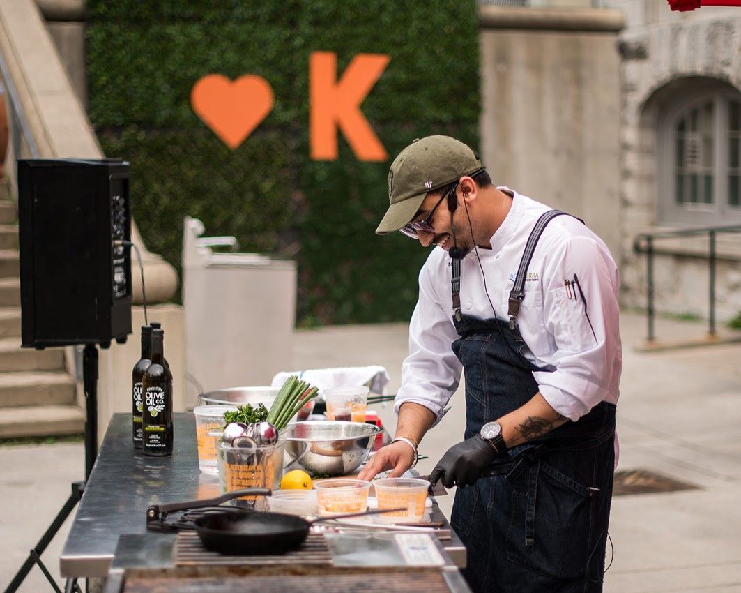 Chef preparing food at an outdoor cooking station with ingredients and equipment.