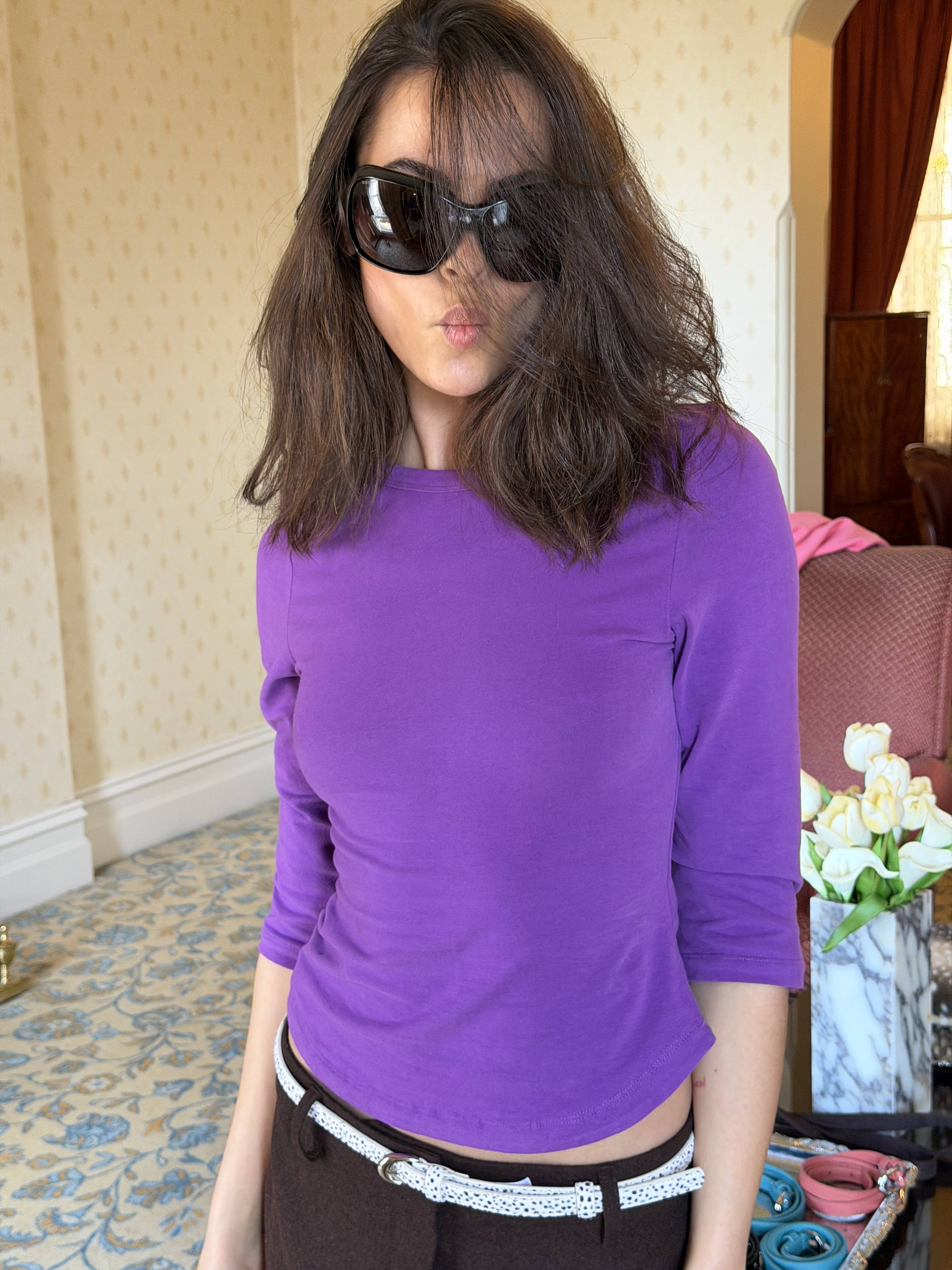 Person in purple top and sunglasses posing indoors.