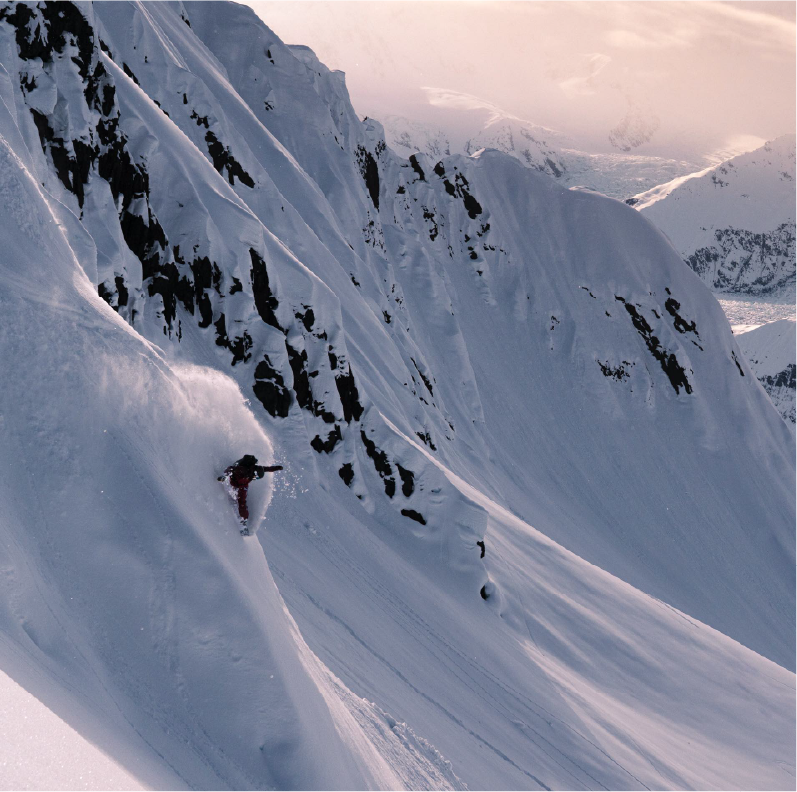 Snowboarder descending a snowy mountain slope surrounded by steep cliffs.
