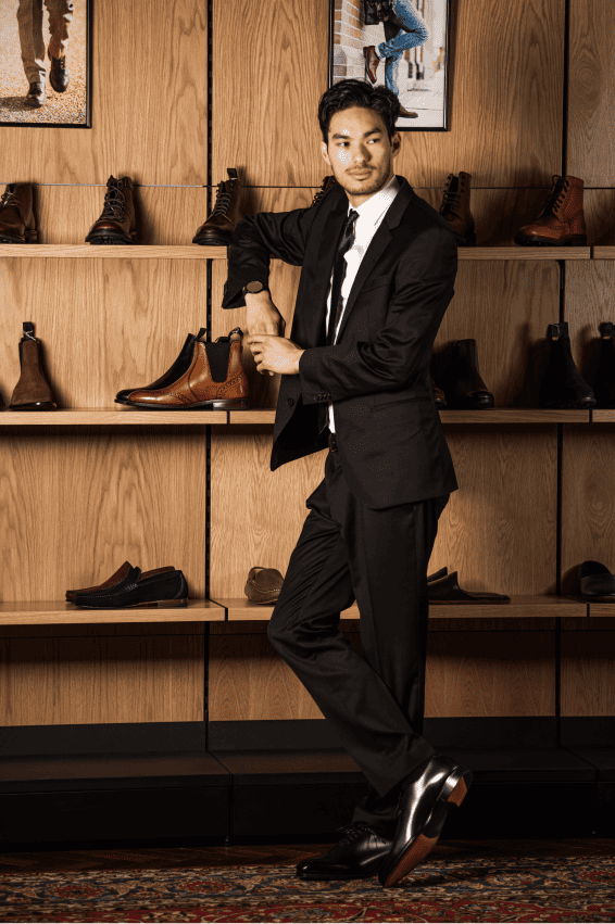 Man in a suit posing beside a shelf of shoes.