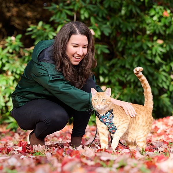 A woman petting an orange cat in a colorful autumn setting.