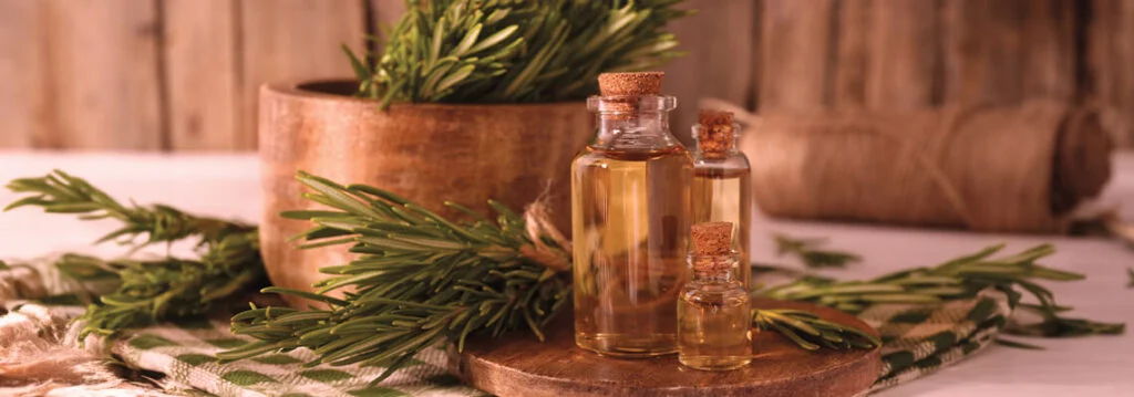 Glass bottle of oil surrounded by fresh herbs and wooden bowls.
