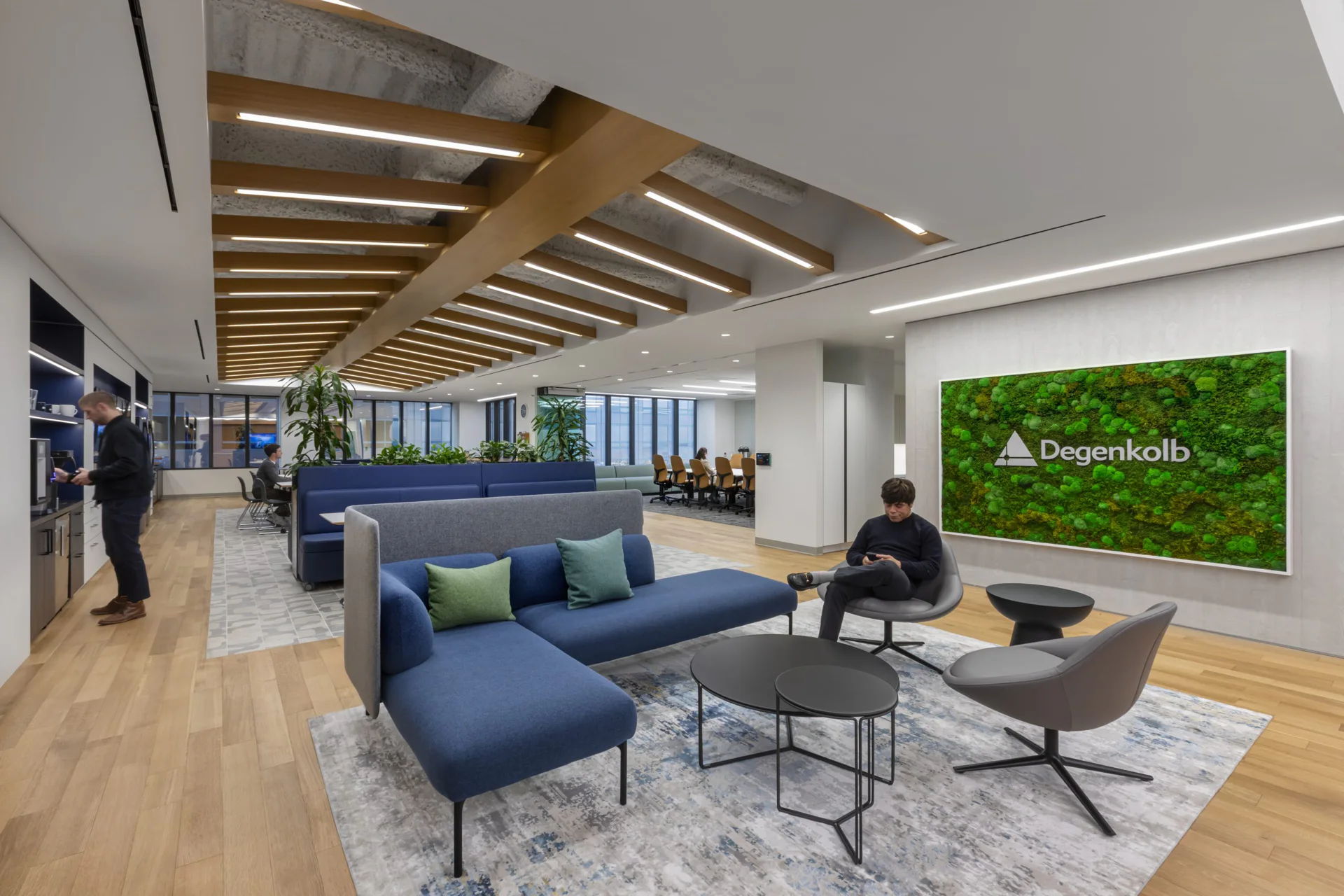 Modern office lounge with seating, plants, and a green wall display.