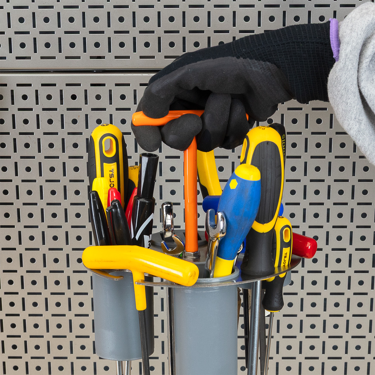 A hand wearing a glove holding tools in a container.