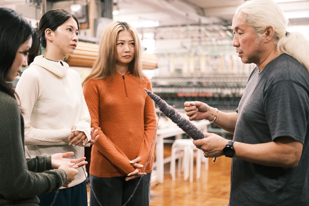 Four people engaged in conversation, with one demonstrating a tool or device.