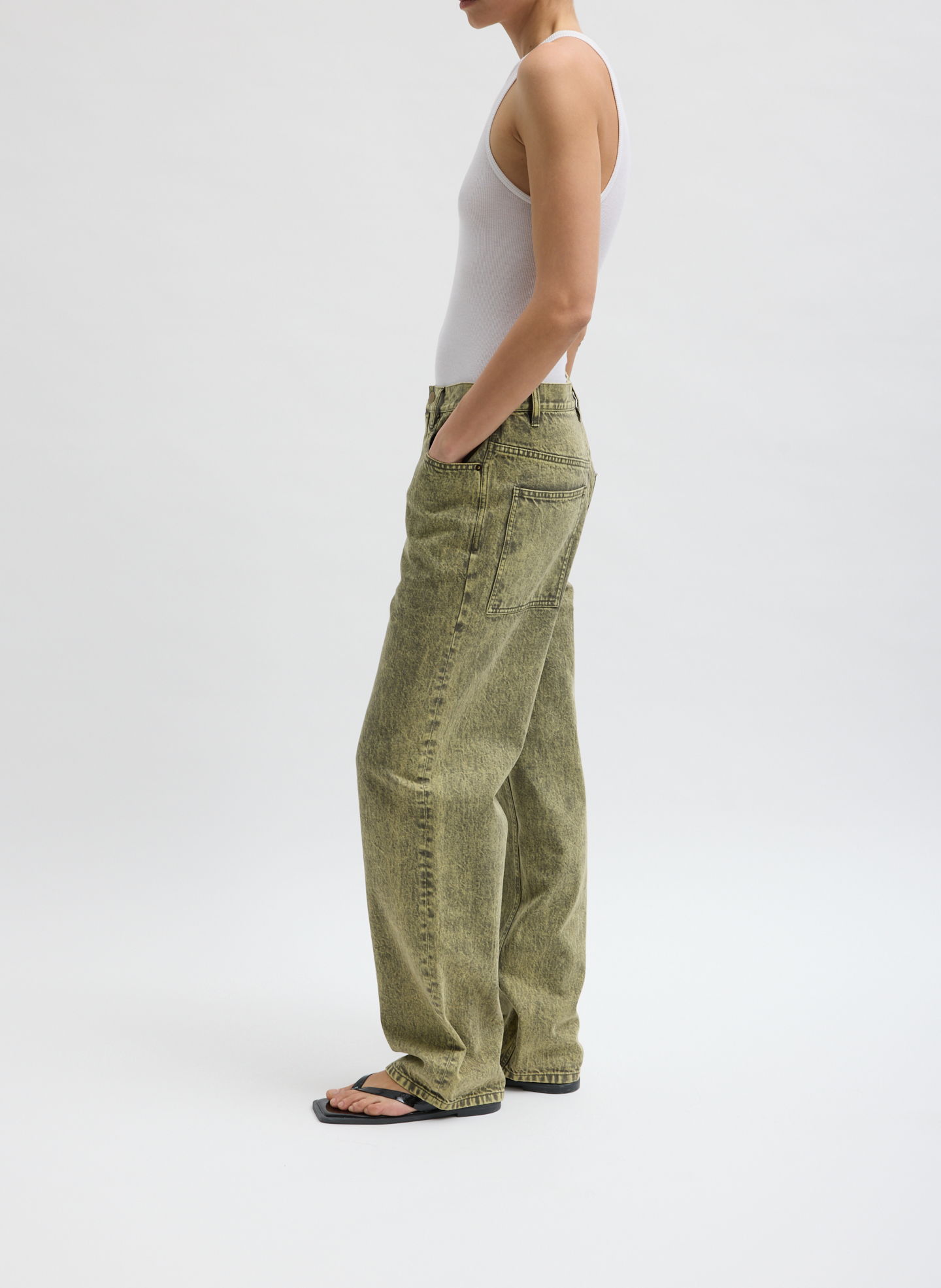 Person wearing a white tank top and olive green pants, standing sideways.