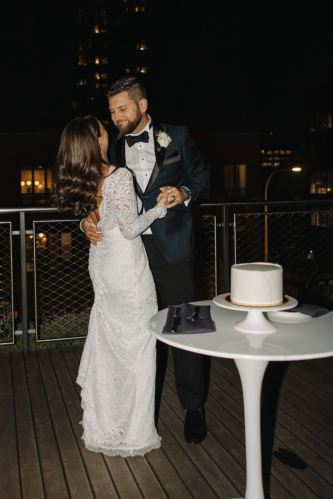 Couple dancing by a table with a wedding cake at night.