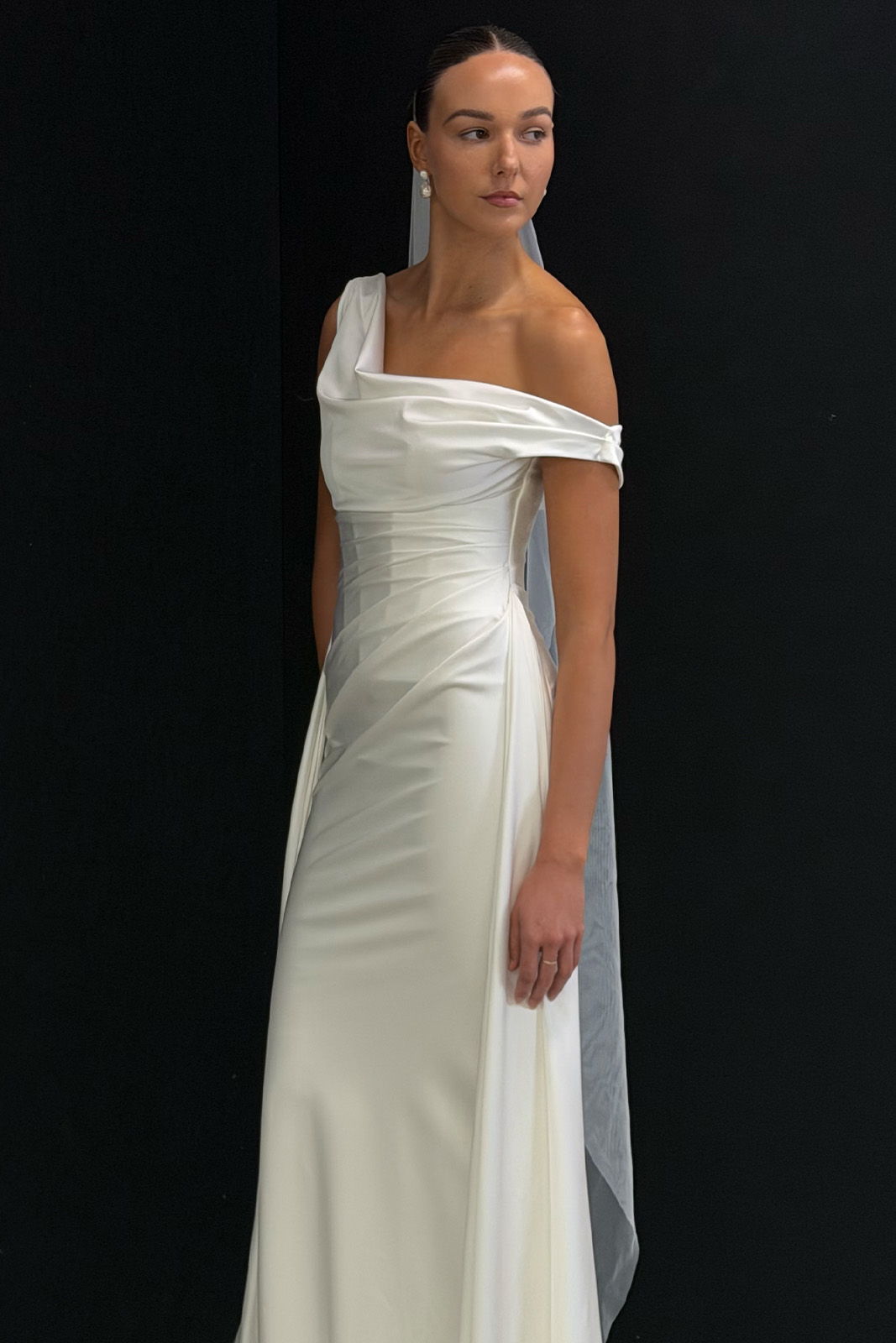 A model in an elegant off-shoulder white gown with a flowing cape.