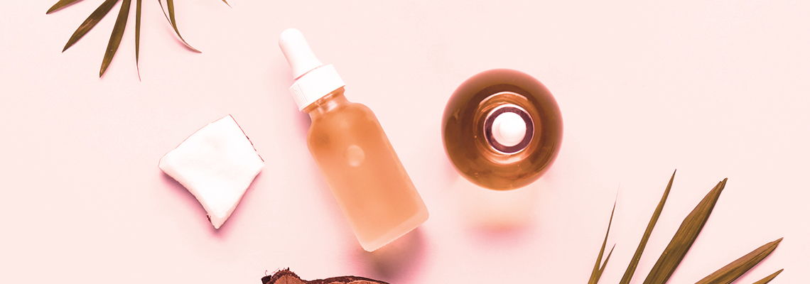 Skincare products on a pink background with tropical leaves.