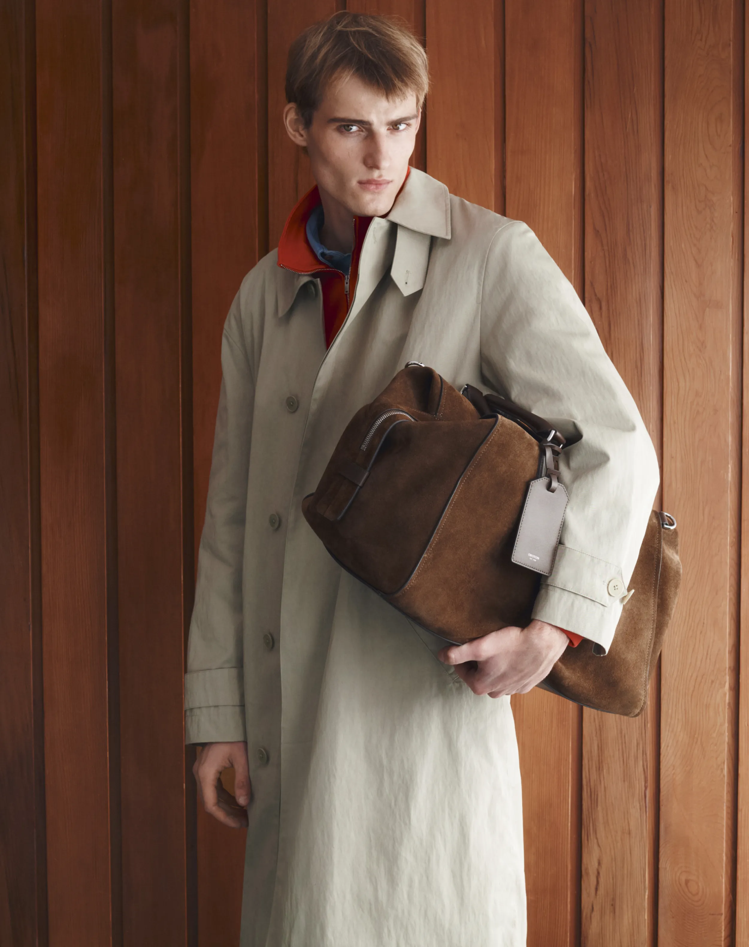 A young man in a trench coat holding a brown bag.