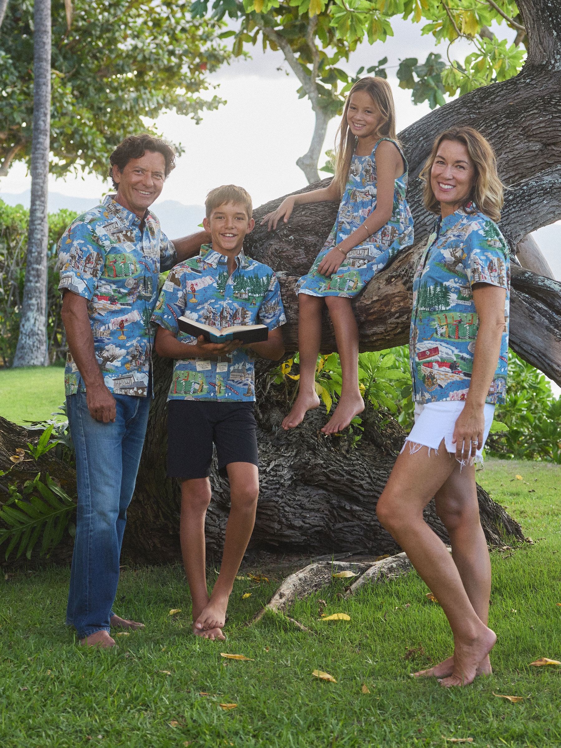 Family posing in matching tropical shirts near a tree.