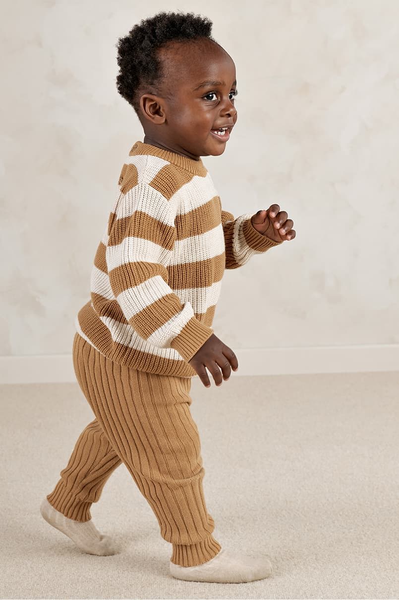A child in a striped sweater and pants walking on a light-colored surface.