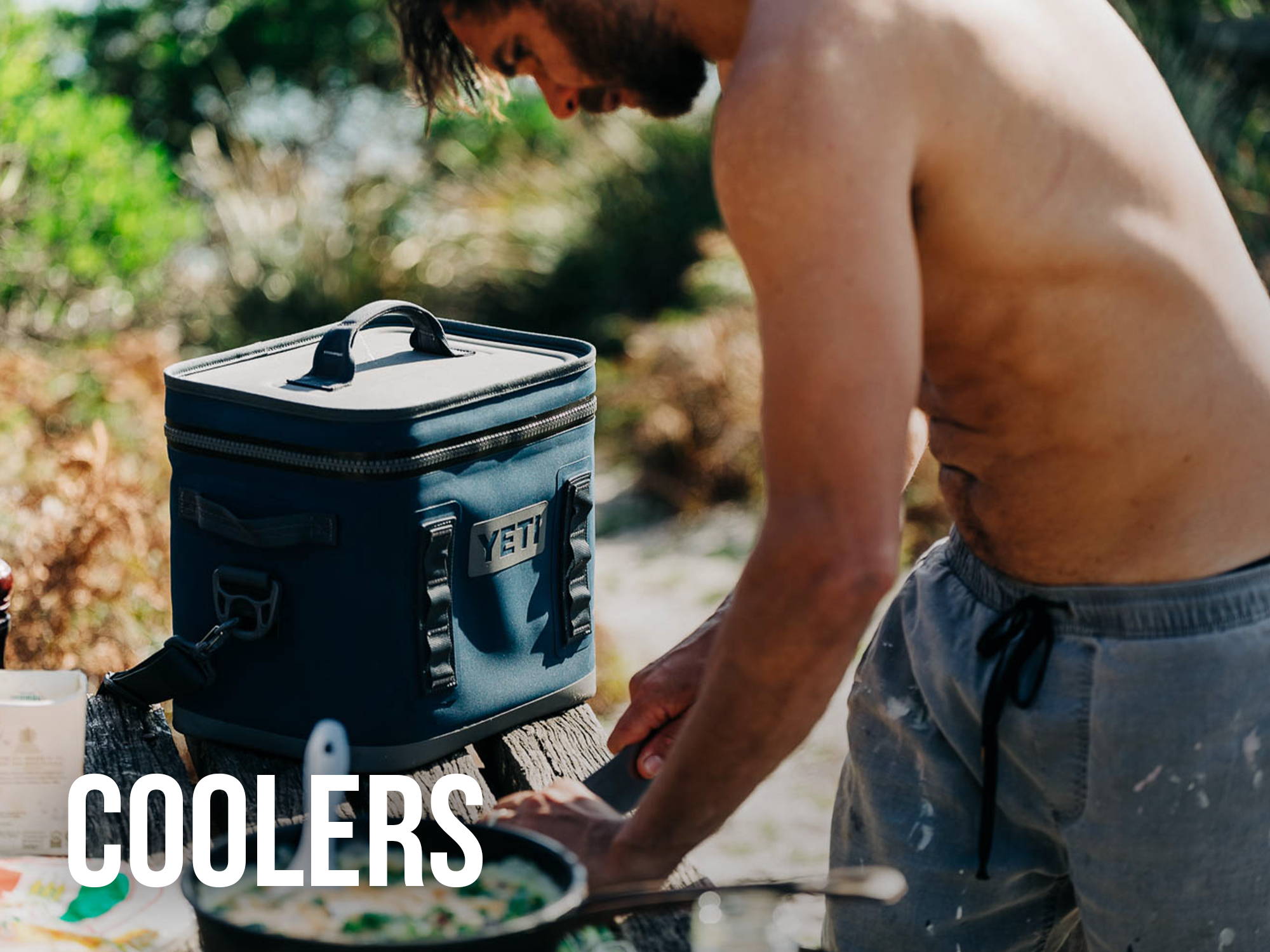 Man in swim trunks preparing food at the beach from Yeti soft cooler