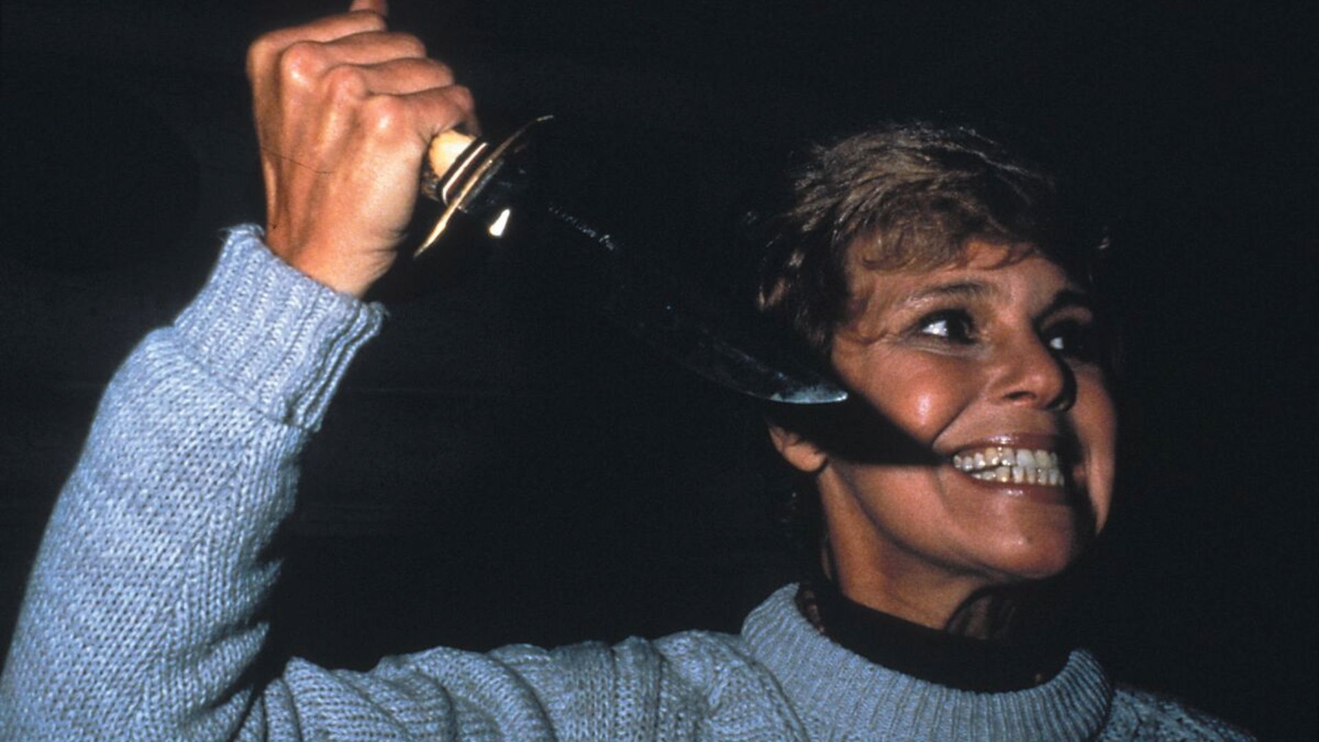 Woman holding a knife, smiling, in a dark background.