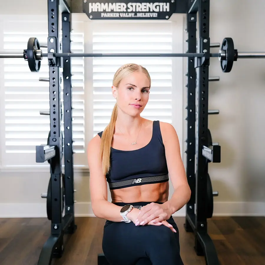 Young woman sitting in front of a weightlifting rack in a gym setting.