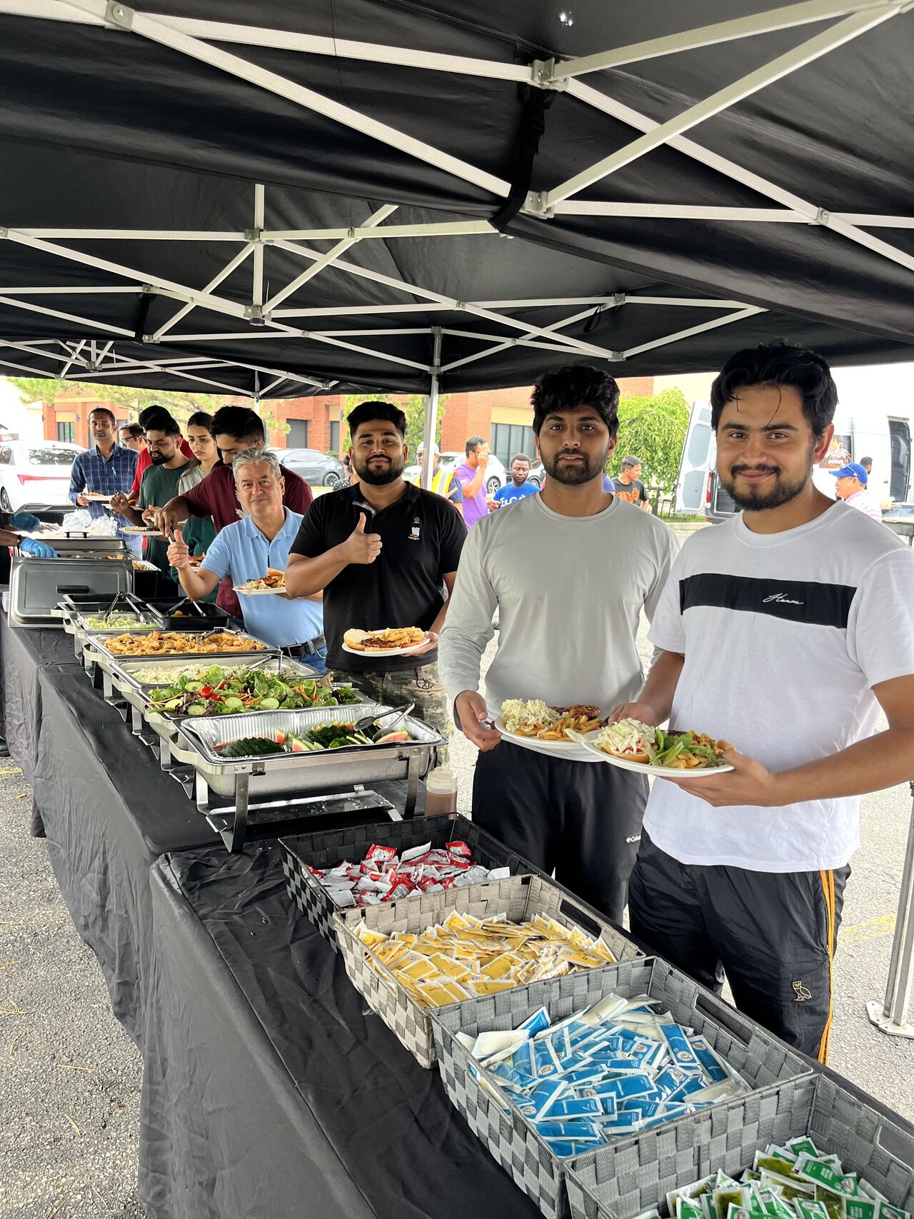 People serving food at an outdoor event under a tent.