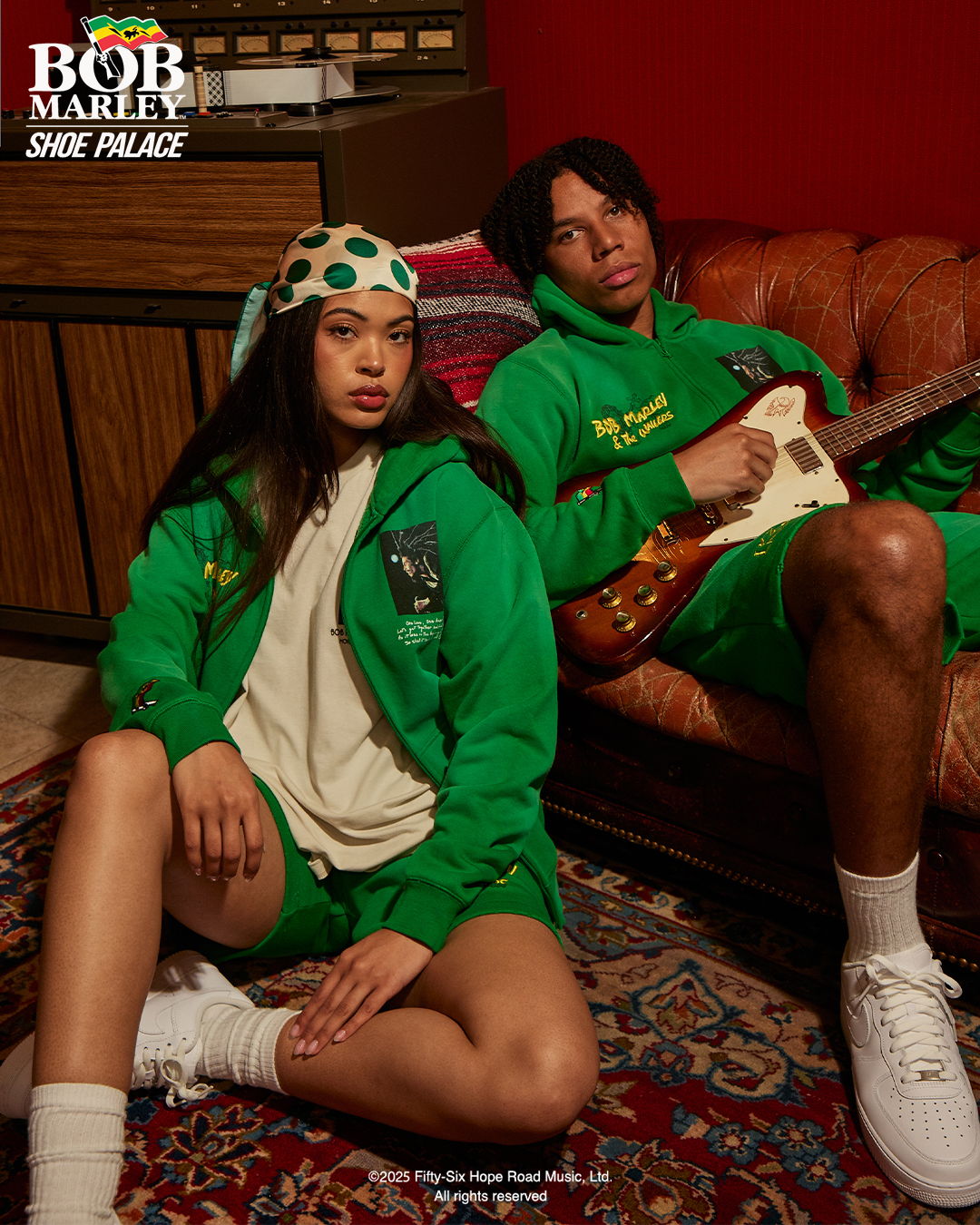 Two individuals in green outfits, one holding a guitar, seated on a rug.
