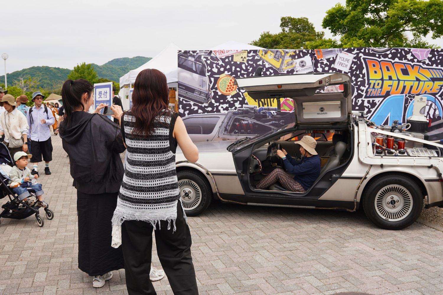 People posing with a DeLorean car at an outdoor event.