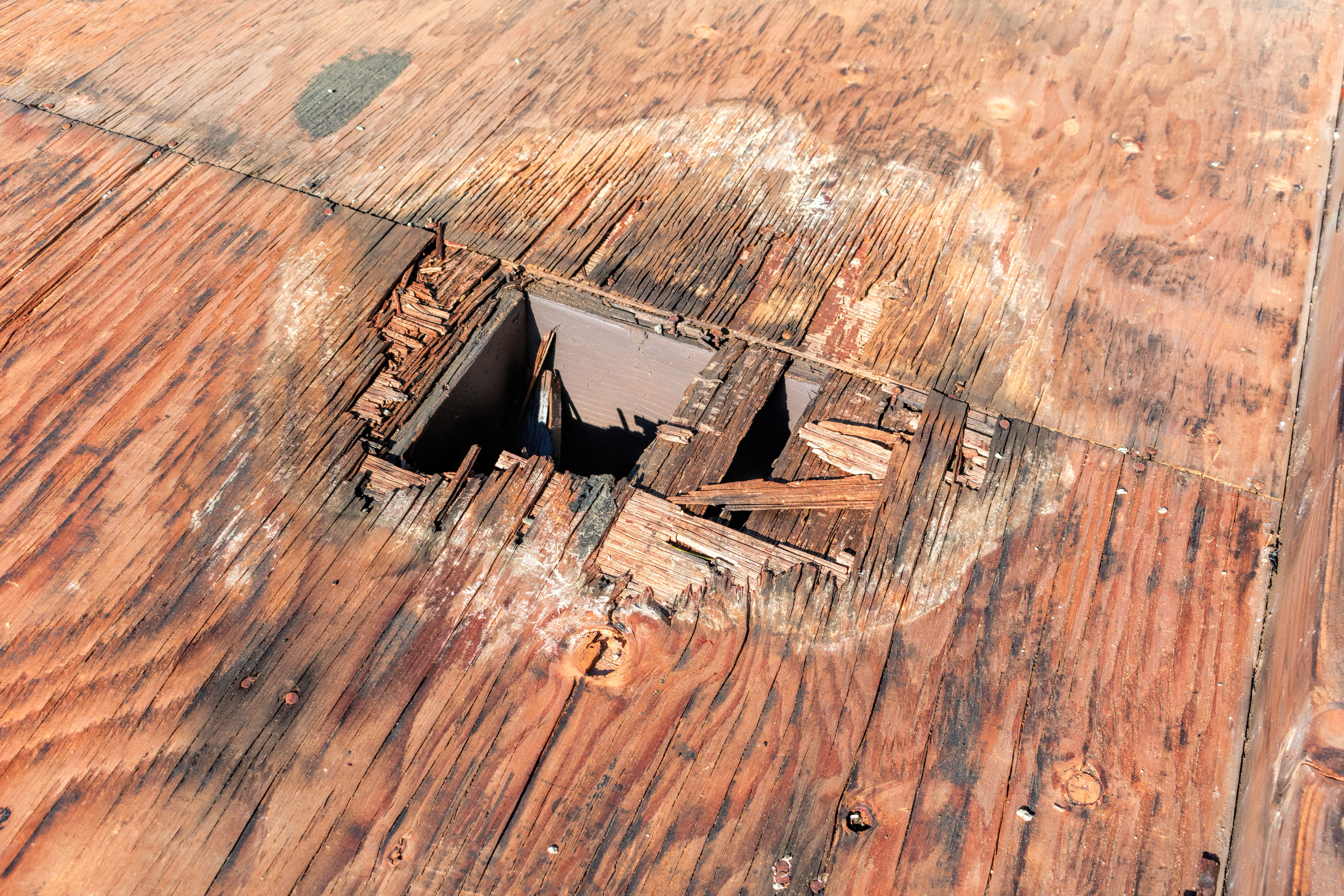A wooden surface with a rectangular hole and surrounding damage.