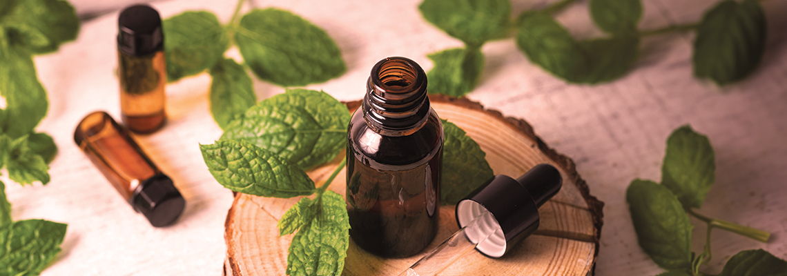 Brown glass bottles on a wooden slice with fresh mint leaves.