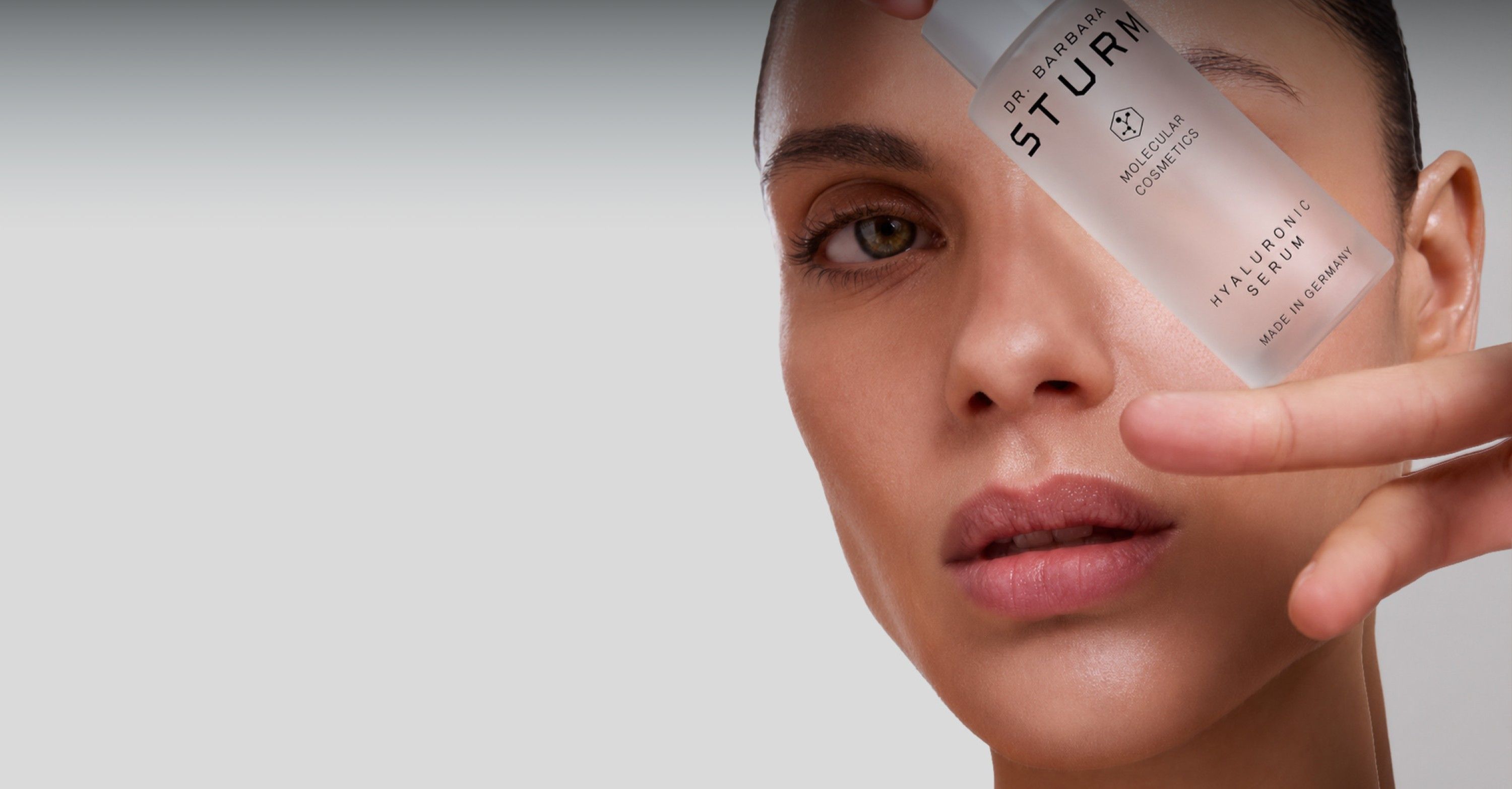 Woman holding skincare product near her face, looking directly at the camera.