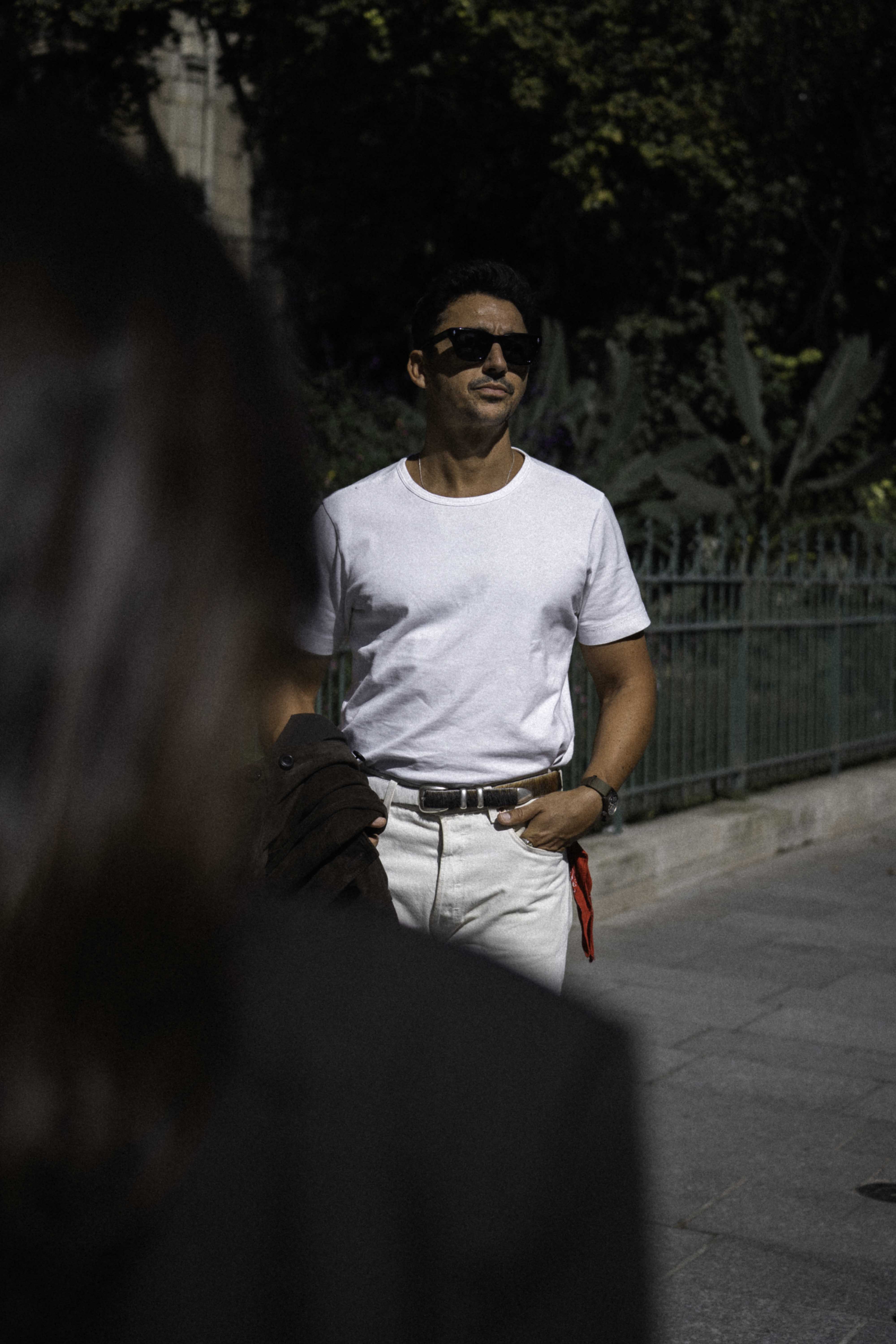 A man in a white shirt and sunglasses standing outdoors.