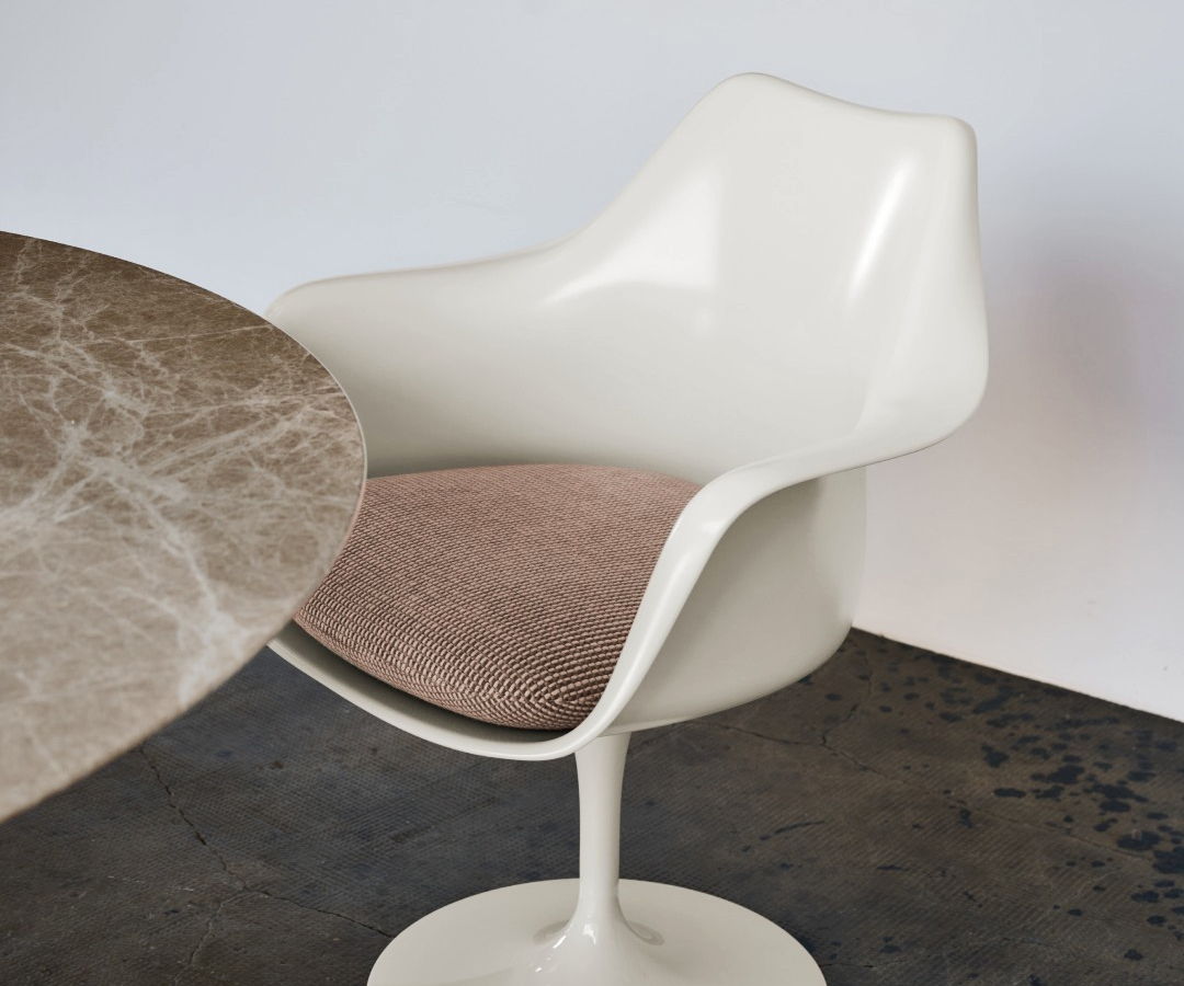 Modern cream Saarinen chair with a pink cushion beside a marble table.