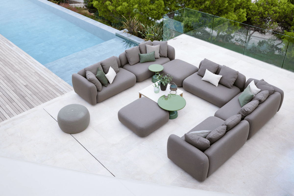 Modern poolside lounge furniture arranged near a pool with modular outdoor seating and low tables.