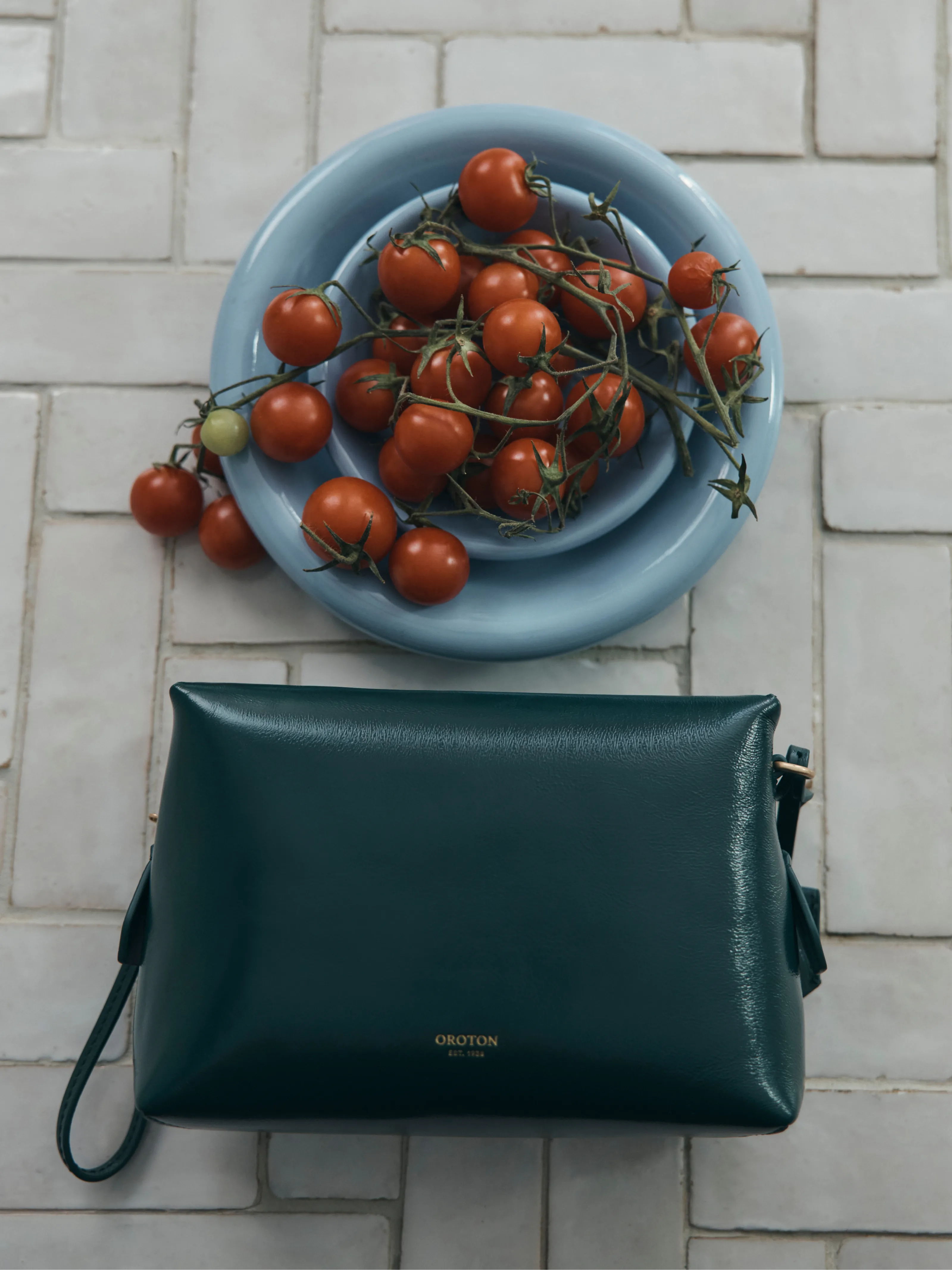 A green bag beside a blue plate of cherry tomatoes on a tiled surface.