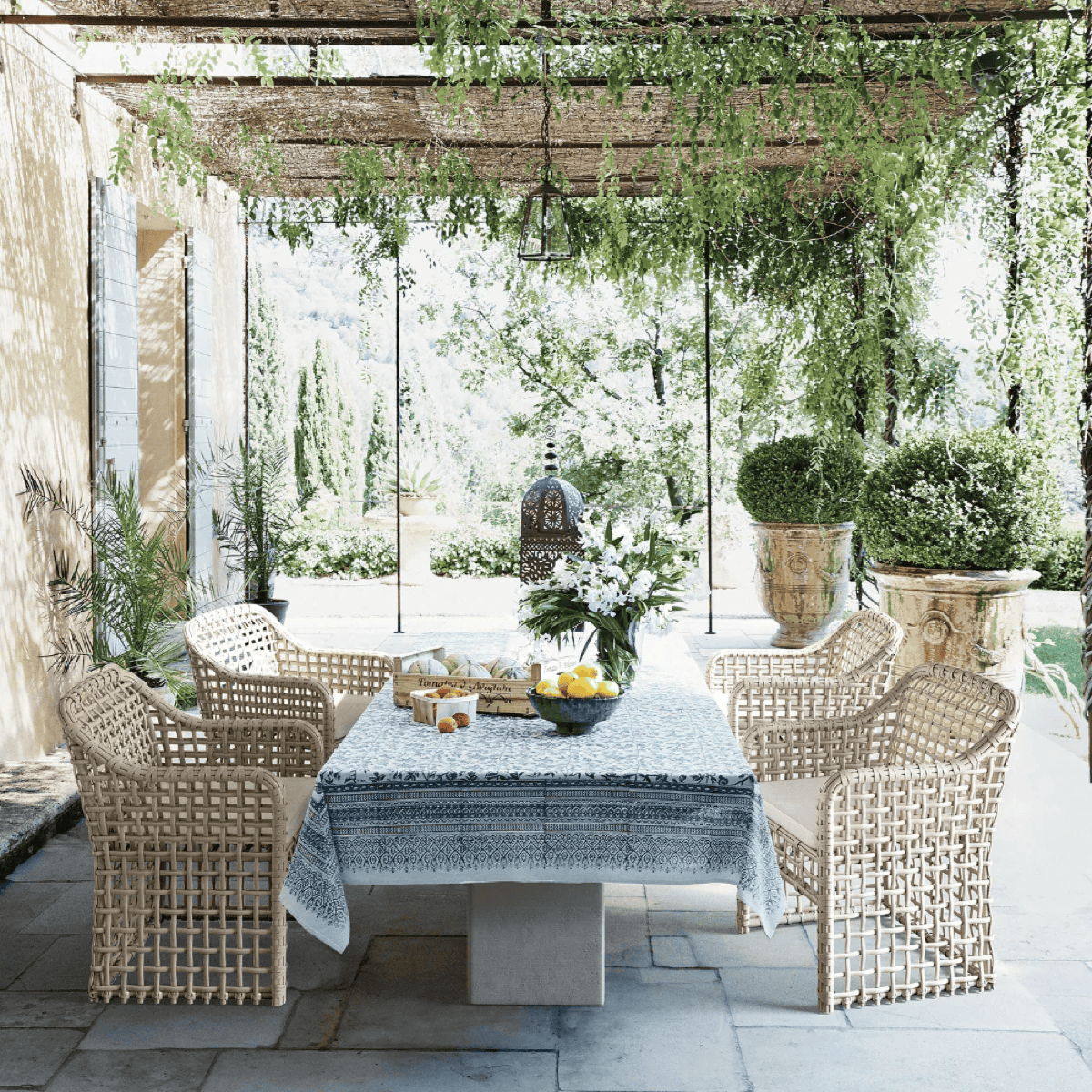 Pergola outdoor dining area with woven dining chairs, stone dining table, greenery, and filtered natural shade.