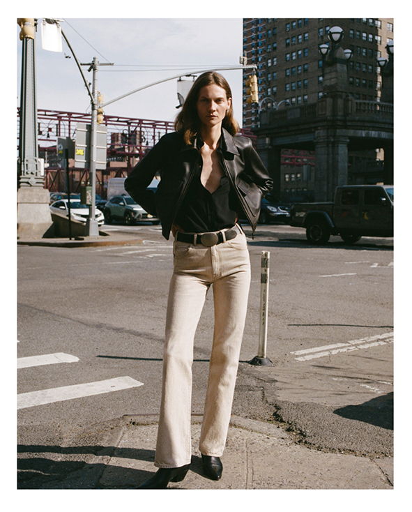 A person wearing a black jacket and beige pants stands on a city street.