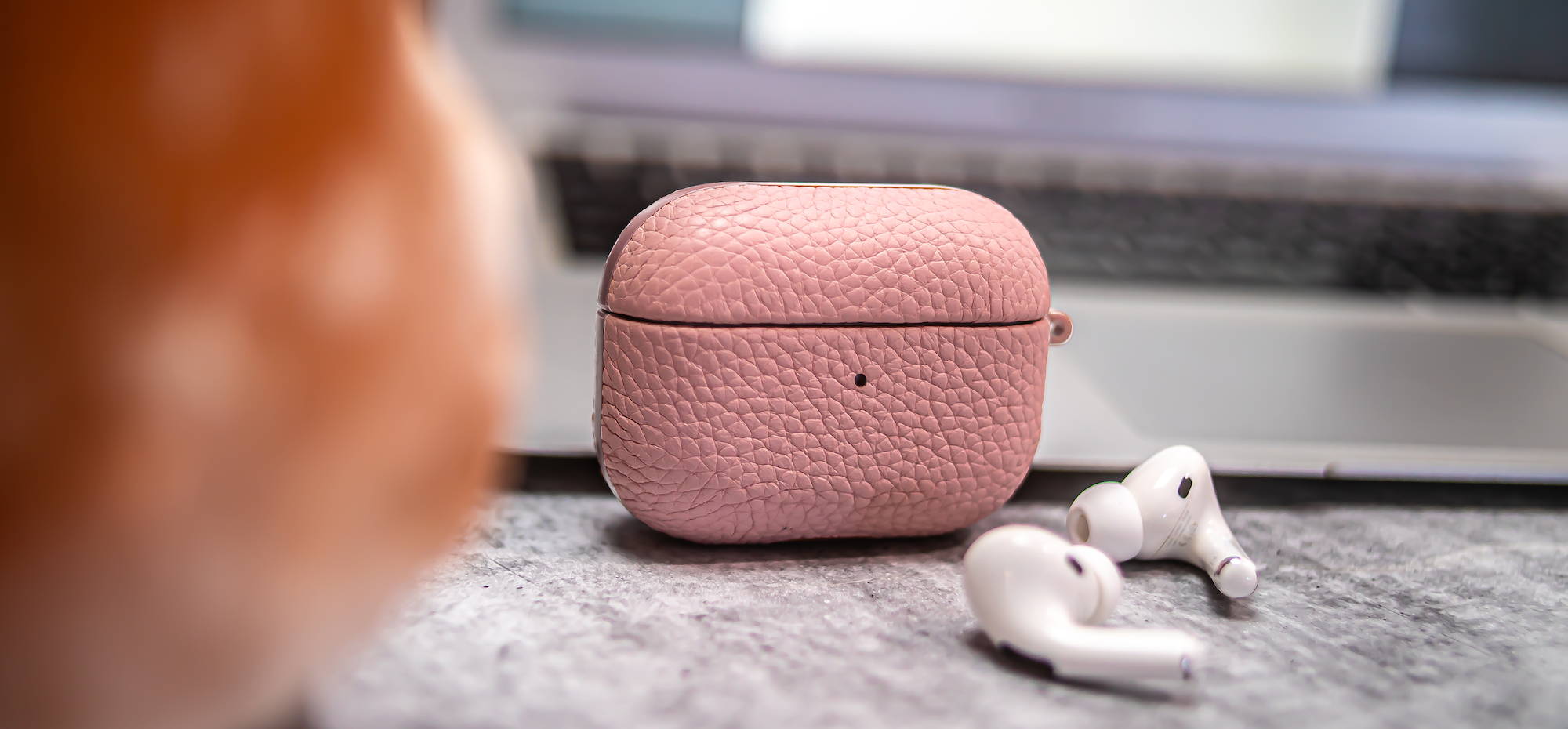 Pink genuine leather airpods pro case on granite table next to a macbook air laptop