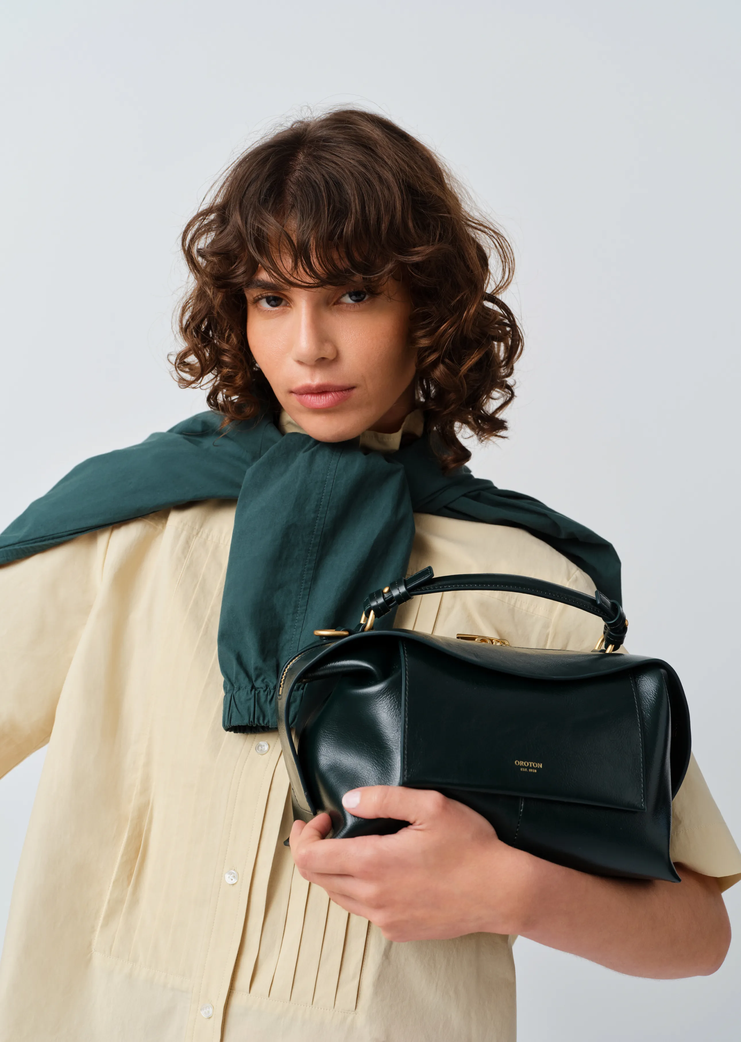 Person with curly hair wearing a light shirt and holding a black handbag.