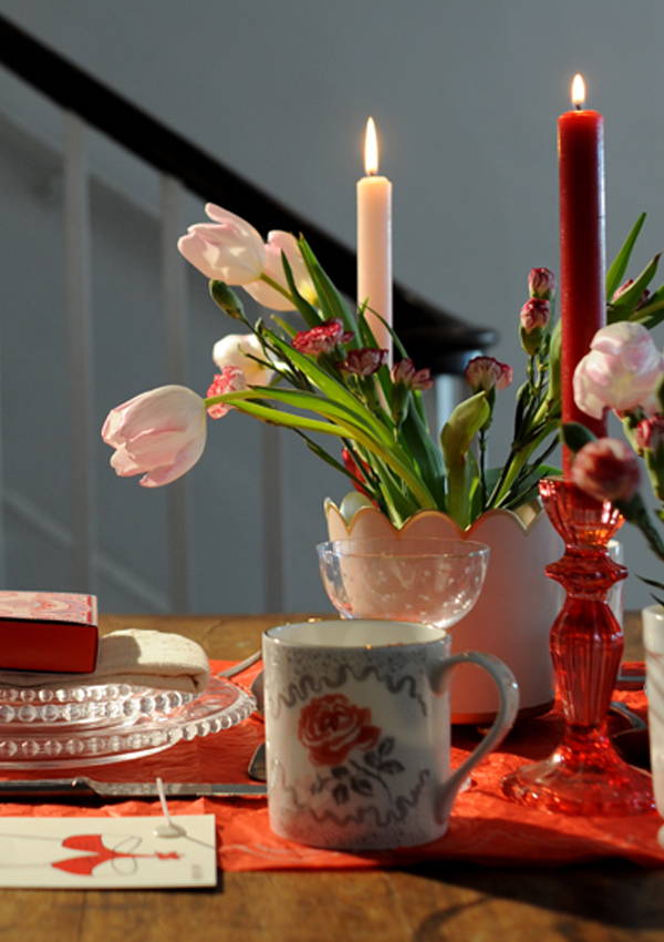 A close up of the table centrepiece of flowers and candles in red and pink.