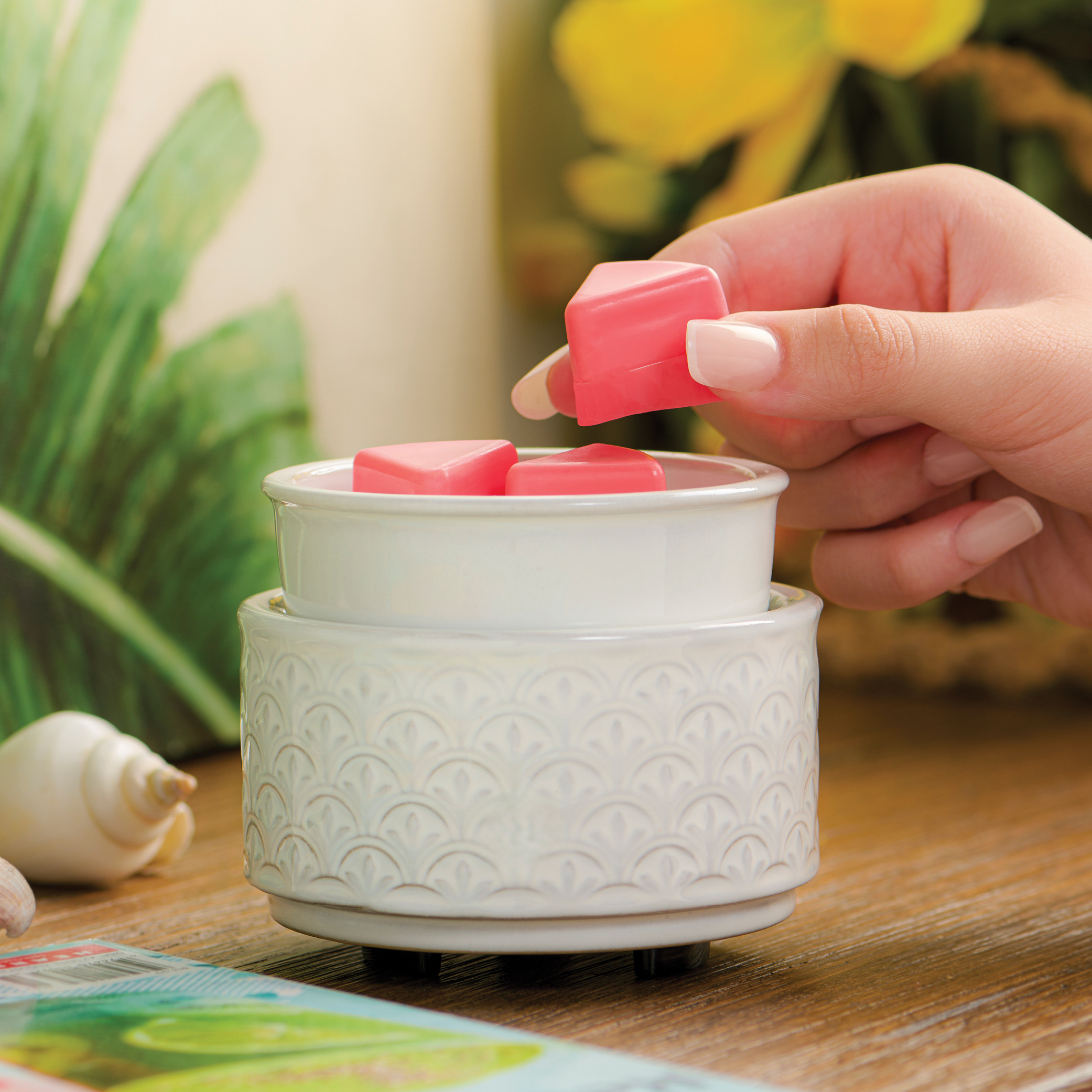 Hand placing pink wax into a decorative wax warmer.