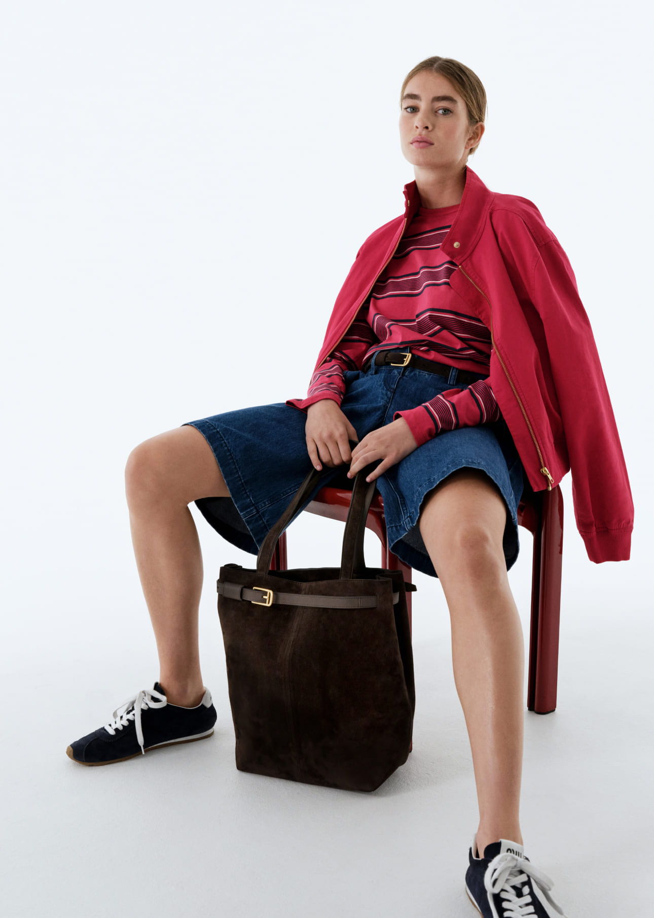 Person sitting on a chair wearing casual attire and holding a bag.