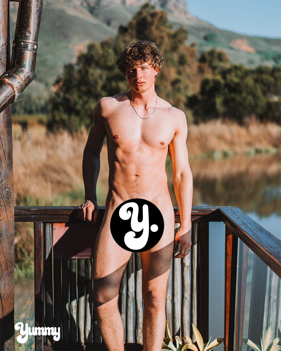 A nude male model standing near a body of water.