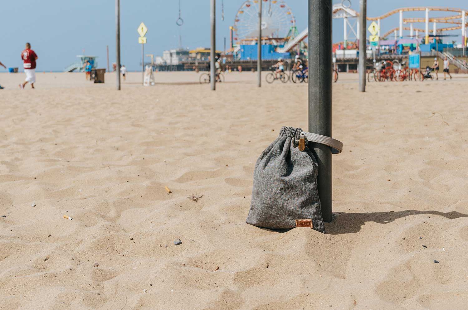 grey anti theft drawstring backpack secured to post at beach