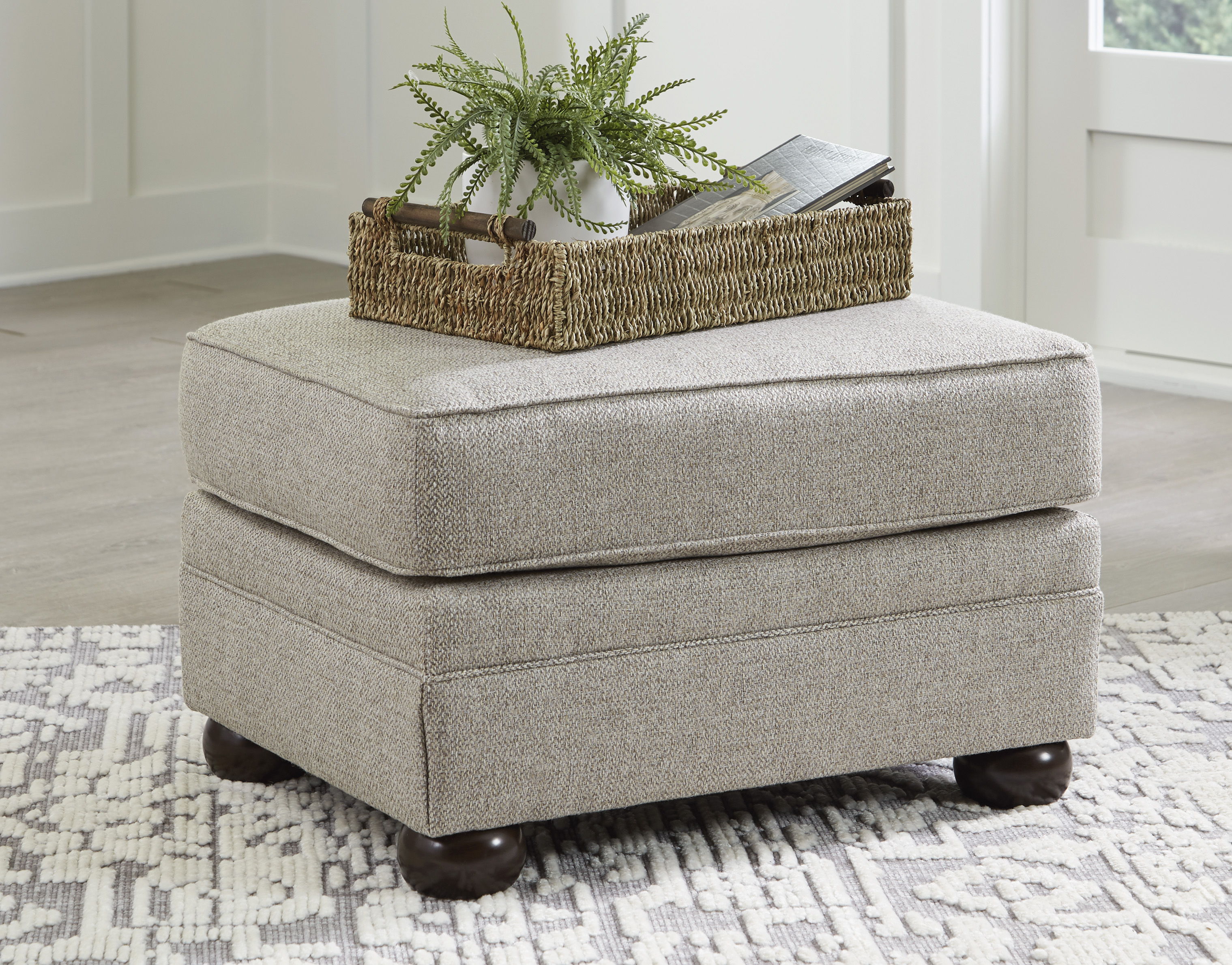 A beige ottoman with a basket and plant on top.