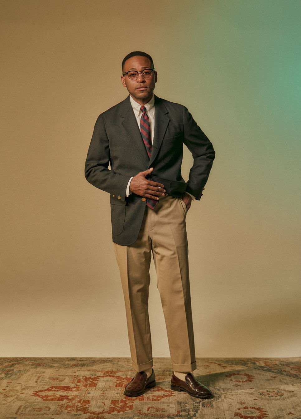 A man in a suit poses confidently against a neutral background.