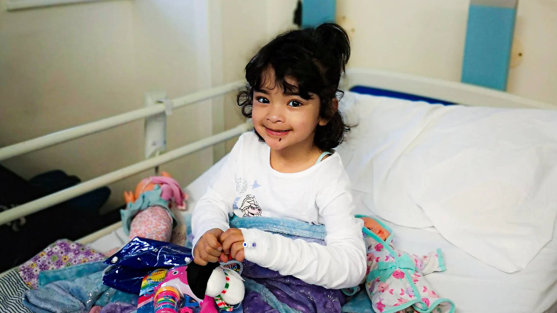 A child with play toys smiling in her hospital bed.