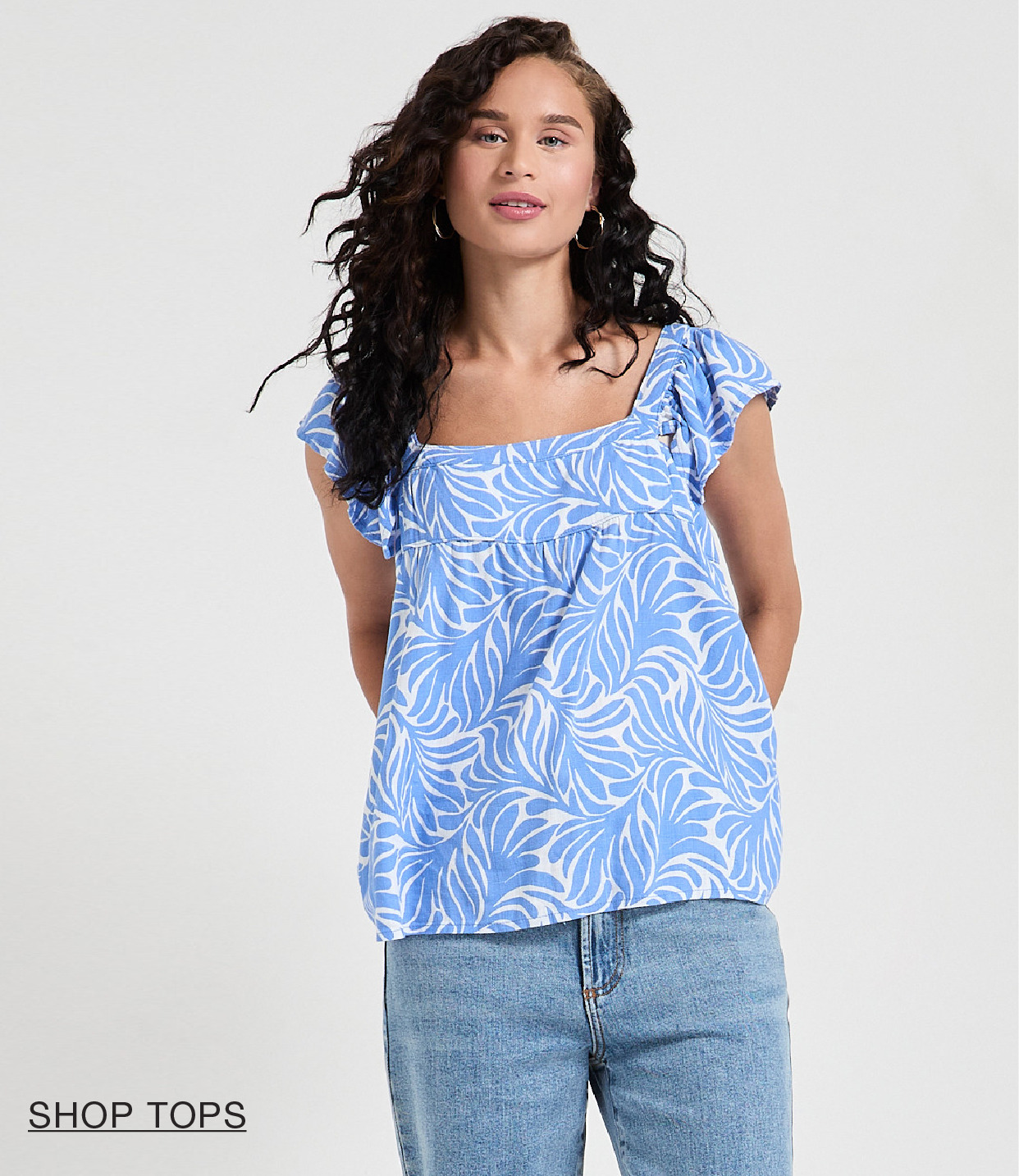 Woman wearing a blue patterned top with ruffled sleeves and jeans.