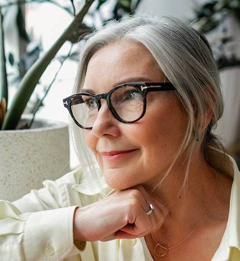 Woman with grey hair wearing thick black round glasses