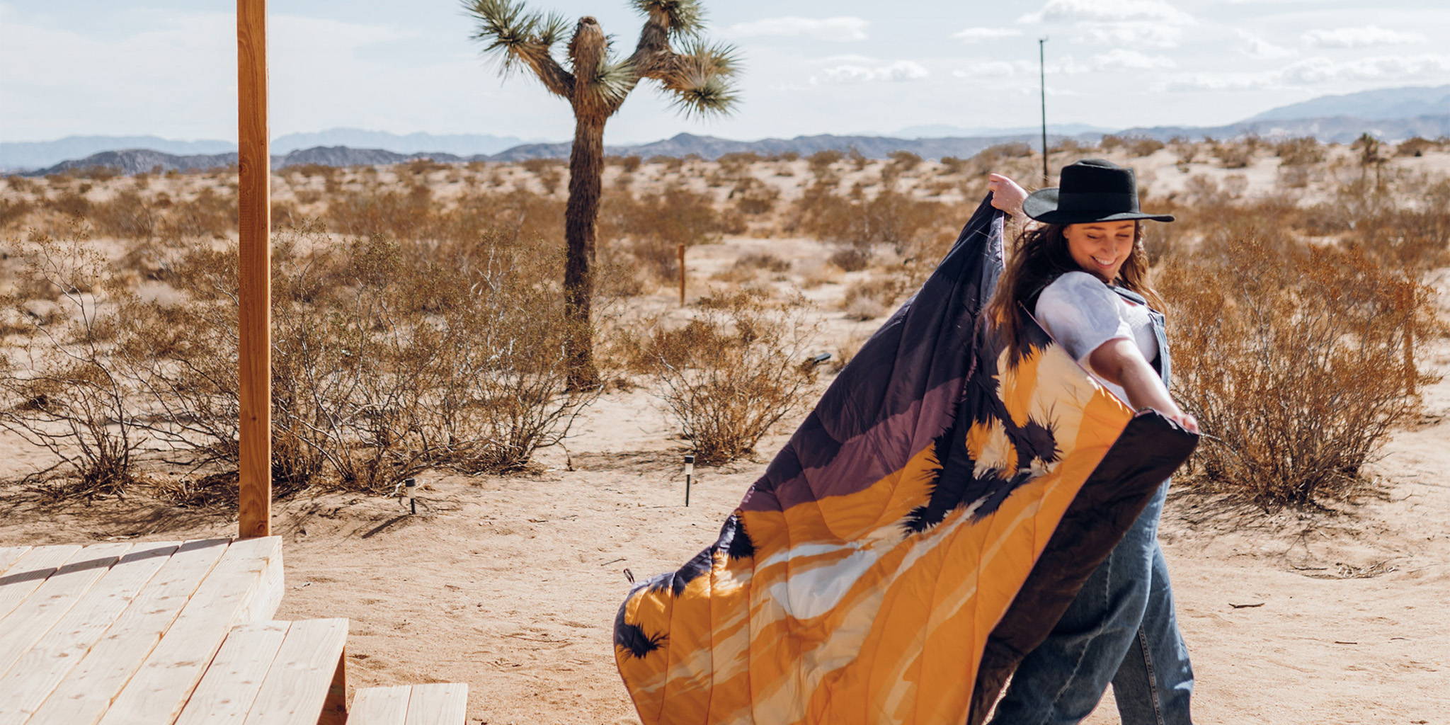 A woman walks through Joshua Tree National Park in California while holding up a Joshua Tree National Park Original Puffy Blanket. 