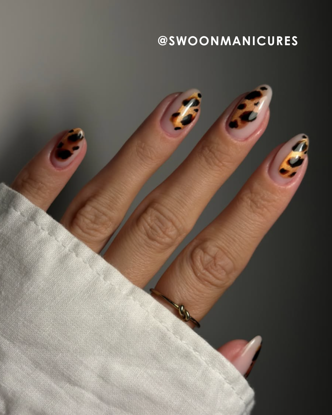 Hand with leopard print nails, partially covered by a white sleeve.
