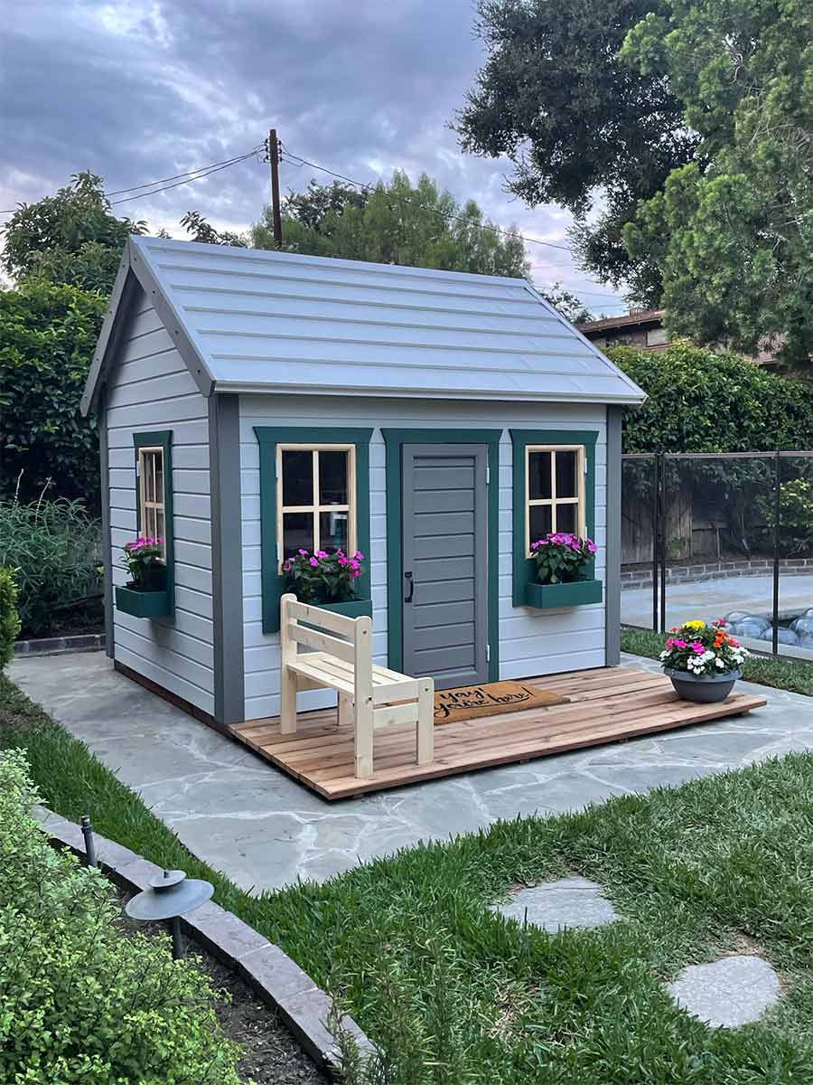 Outdoor Playhouse Natural Wonder with gray metal roof and green flower boxes with wooden teracce in a backyard by WholeWoodPlayhouses 