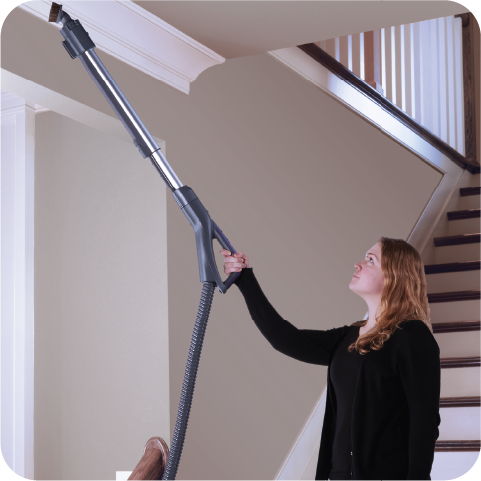 Woman using a long cleaning tool to reach a ceiling.