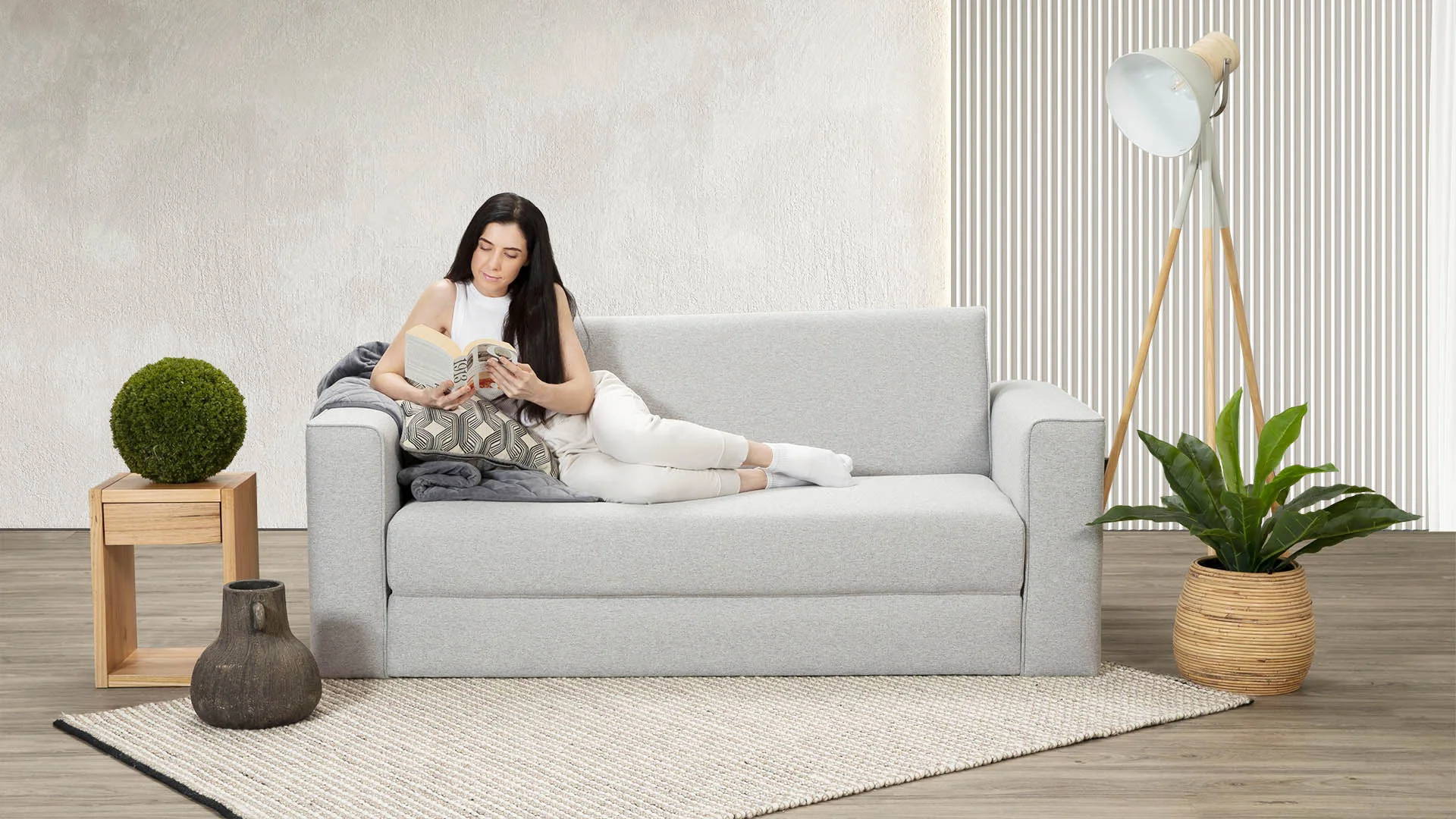A woman lounging on a new Zeek Silver Sofa Bed reading a book.